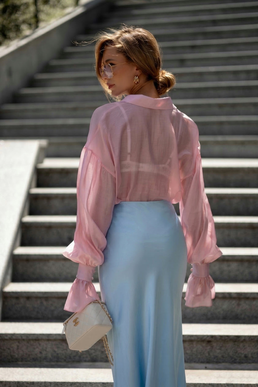 Woman wearing a pink blouse and light blue skirt standing on steps.