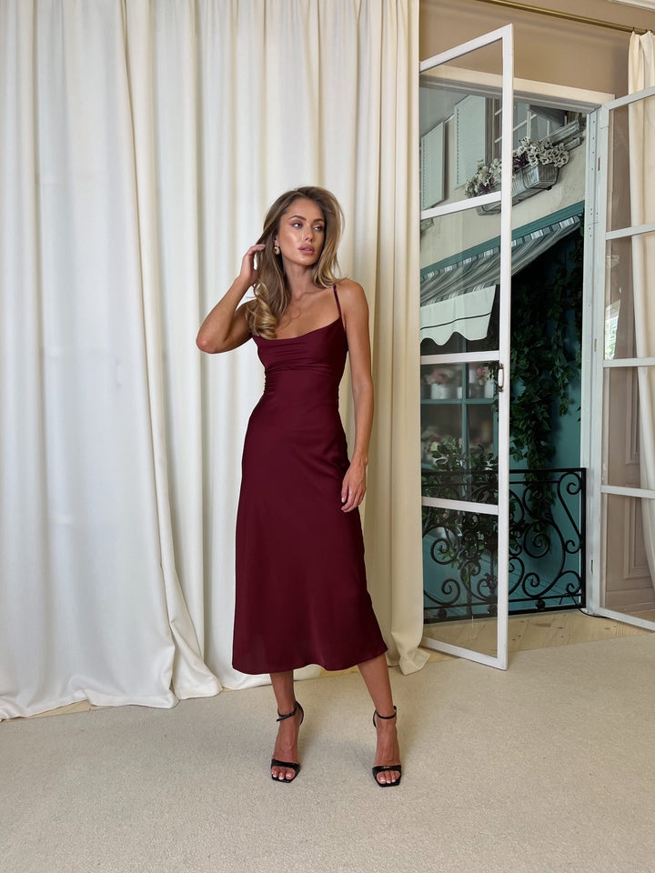 Burgundy silk satin cowl neck slip dress, full-length front view with fitted waist, smooth satin sheen and bias-cut midi skirt that flares gently at the hem.