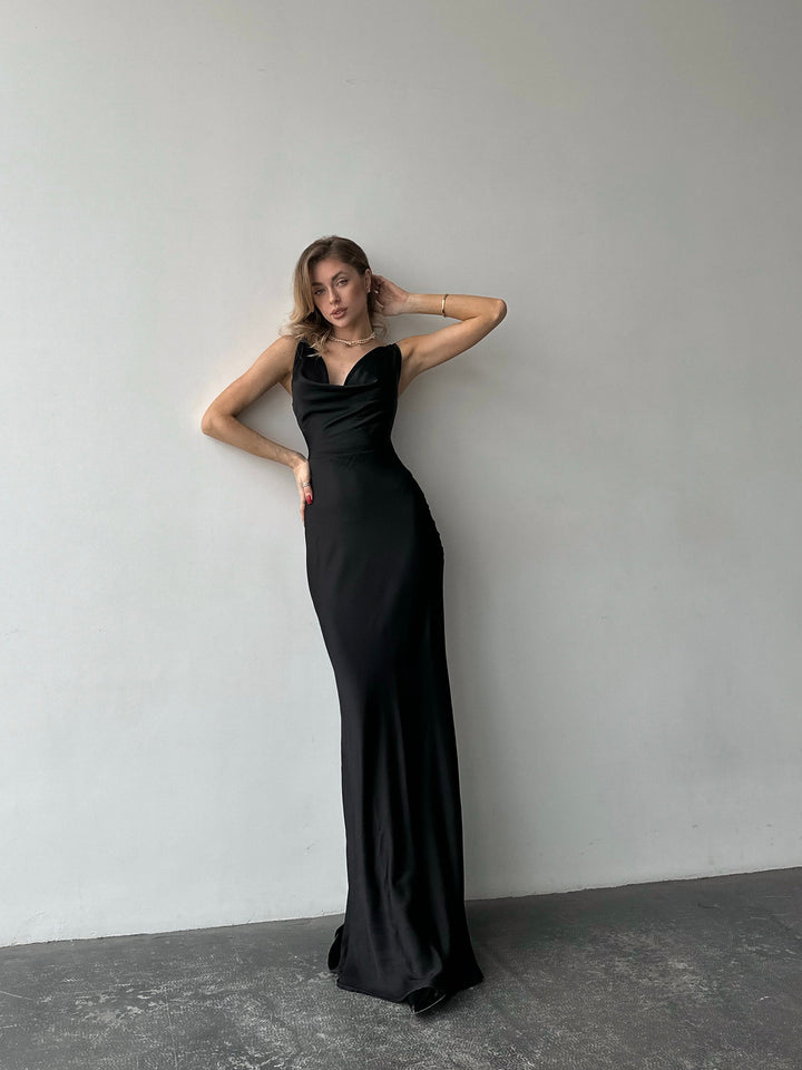 Woman in a black evening gown standing against a plain white wall.