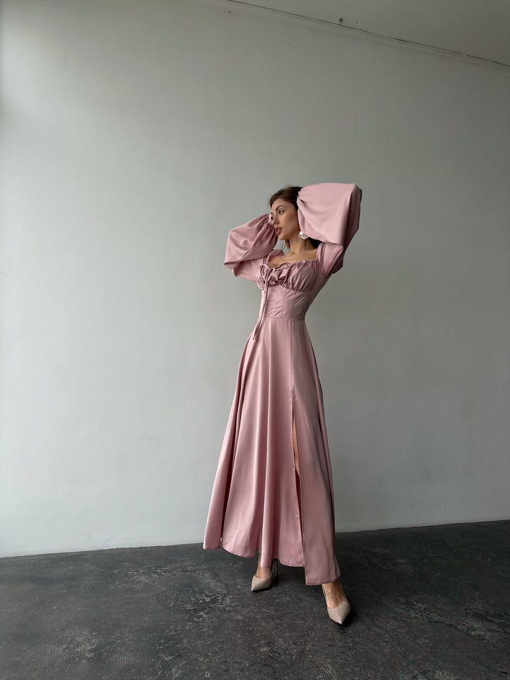 Woman modeling a trendy blush pink silk maxi gown with voluminous sleeves and a thigh-high slit. A luxurious look for an evening reception.