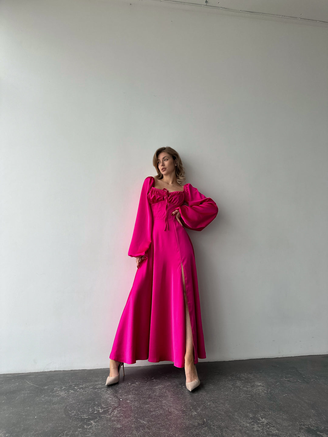 Bright pink floor-length satin dress showcasing versatile draped sleeves and a leg slit. A feminine silhouette perfect for a chic summer wedding guest.