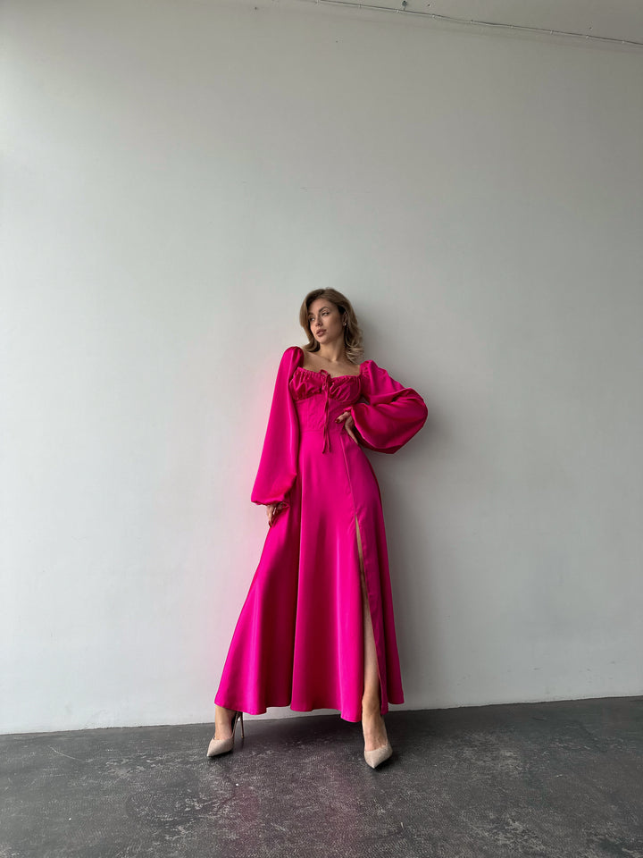 Bright pink floor-length satin dress showcasing versatile draped sleeves and a leg slit. A feminine silhouette perfect for a chic summer wedding guest.