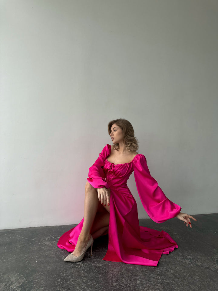 Romantic bright pink satin maxi dress showcasing versatile bishop sleeves and a sweeping skirt with a thigh slit. Ideal for an elegant formal gathering.