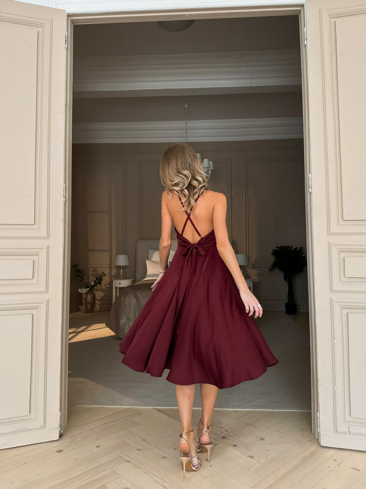 Burgundy silk slip midi dress with deep V-neck and open bow back — back view