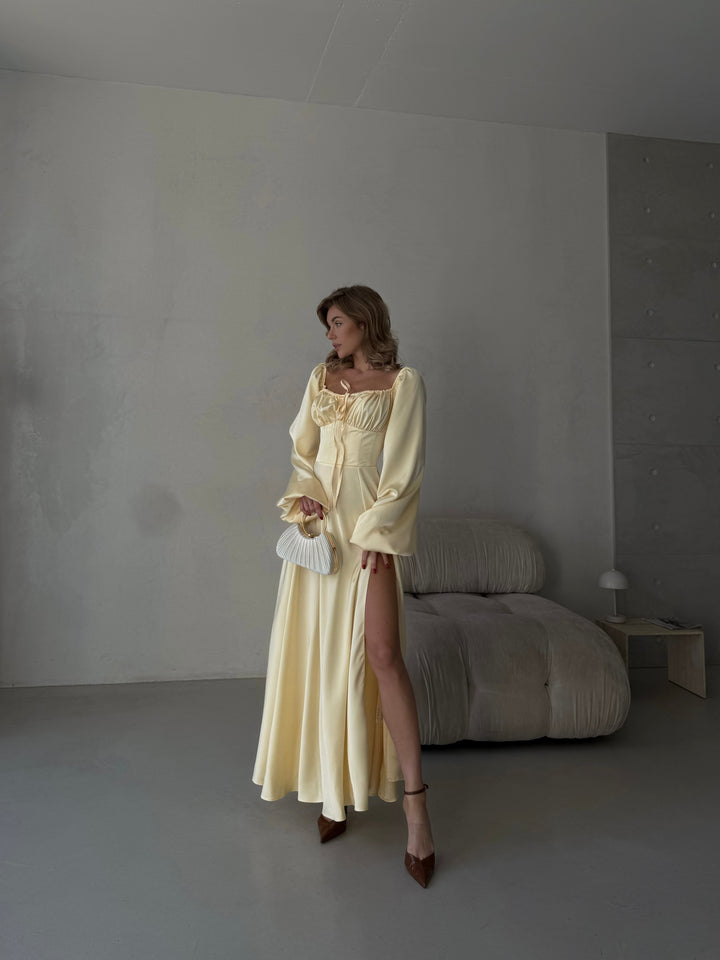 Sophisticated light yellow satin dress offering long cuffed sleeves, a fitted bodice, and a high slit maxi skirt. Perfect for a summer wedding guest or formal evening.