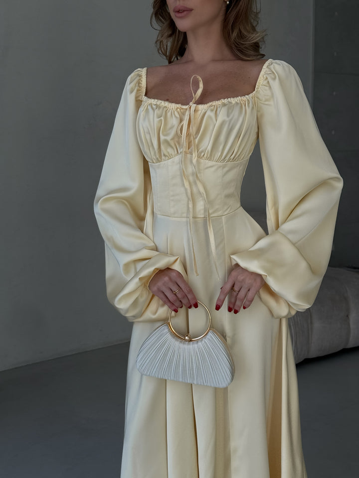Long-sleeve butter yellow silk-blend dress highlighting a fitted bodice and a sweeping maxi skirt with a side slit. Ideal for an upscale cocktail party or gala.