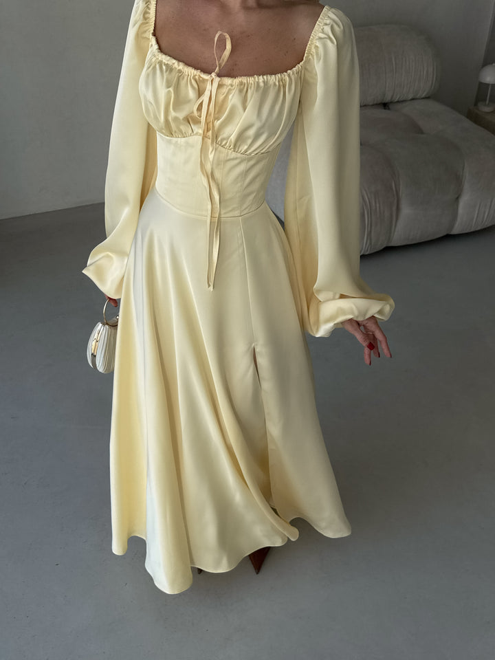Woman wearing a light yellow silk formal dress showcasing voluminous bishop sleeves and a thigh-high slit. A stunning look for a summer wedding guest or evening reception.