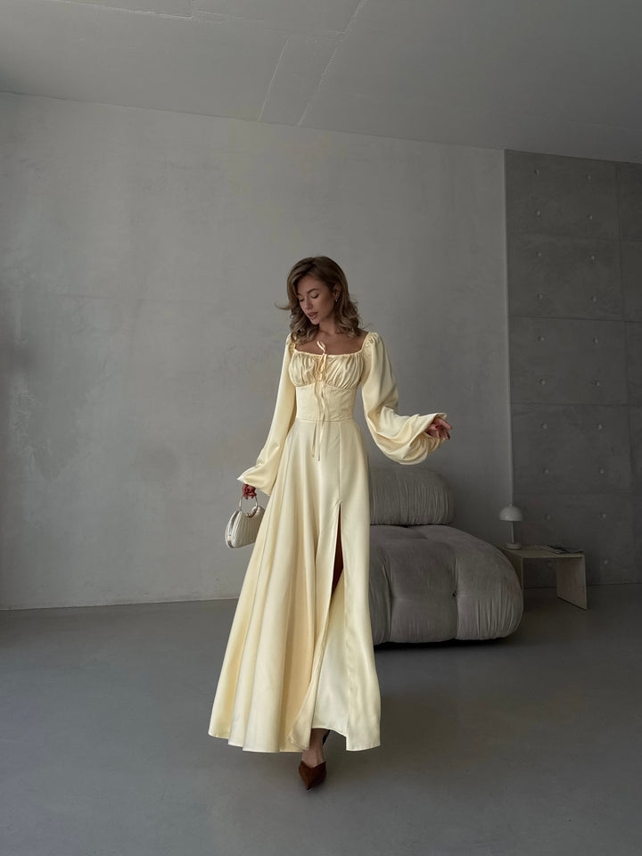 Luxurious butter yellow silk maxi dress with off-the-shoulder long sleeves, a sweetheart cut, and a dramatic front slit. Perfect for an elegant cocktail party look.