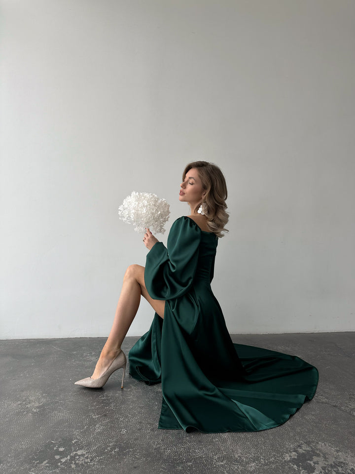 Romantic dark green satin maxi dress showcasing versatile bishop sleeves and a sweeping skirt with a thigh slit. Ideal for an LA style event.