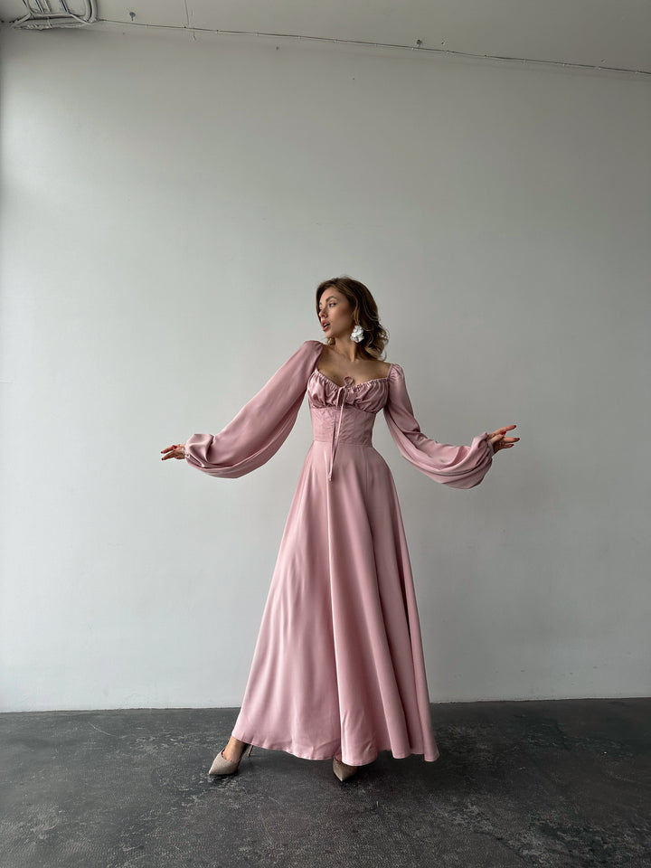 Elegant dusty pink silk maxi dress featuring long bishop sleeves and a side slit. A sophisticated choice for a spring wedding guest outfit.