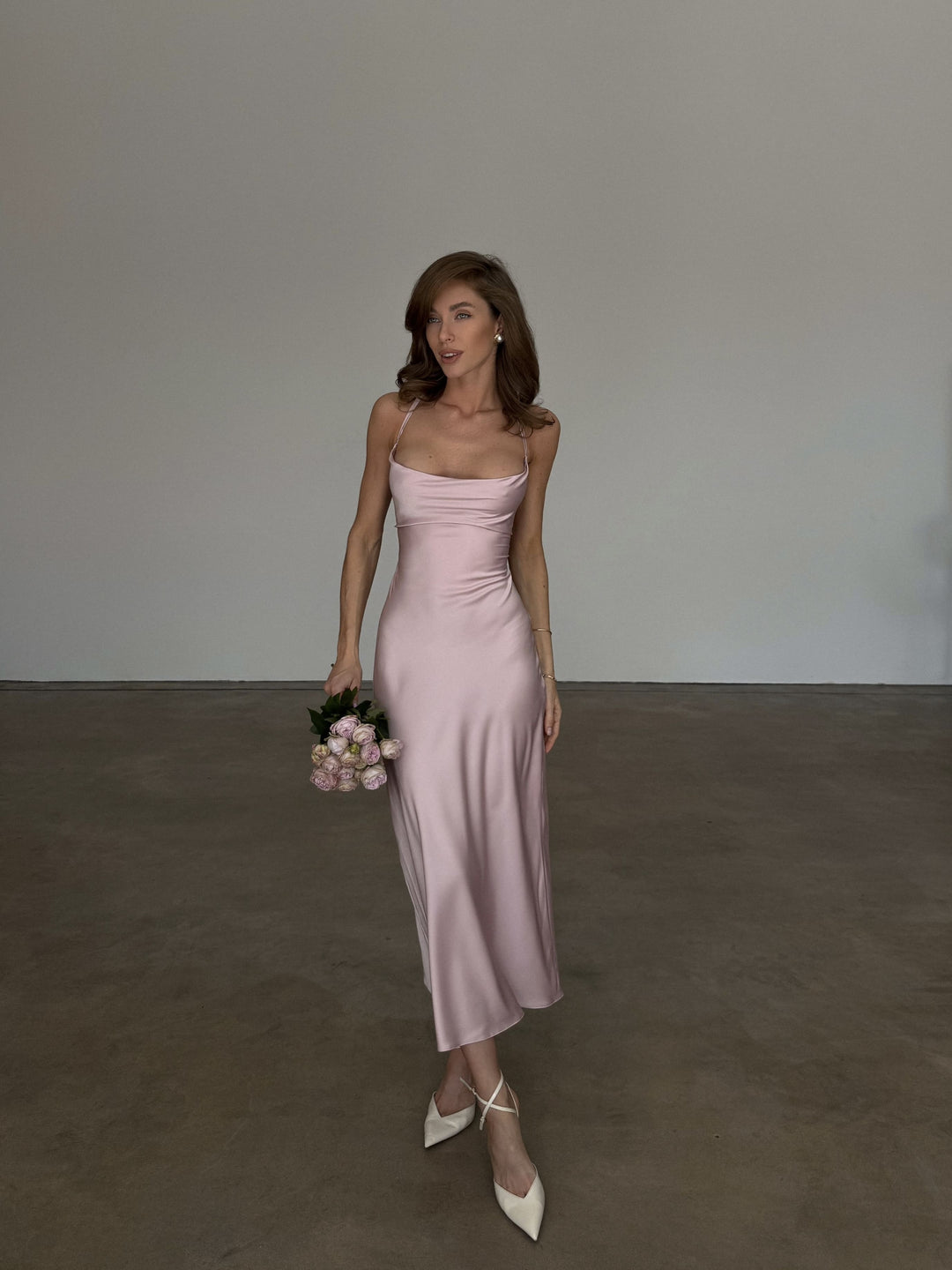 Dusty pink silk satin slip dress, full-length front walking shot: cowl neck, crossed thin straps, bias-cut midi length moving at the hem, ivory pointed heels.