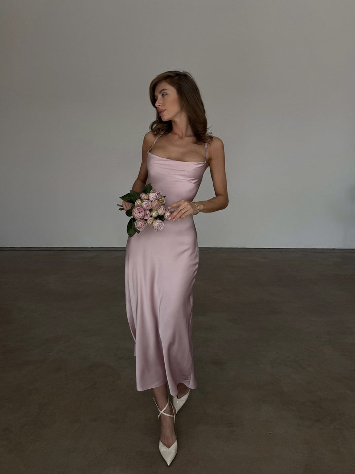 Dusty pink silk satin slip dress, full-length front view: cowl neck, spaghetti straps, bias-cut midi skirt and ivory pointed slingback heels, holding a small rose bouquet.