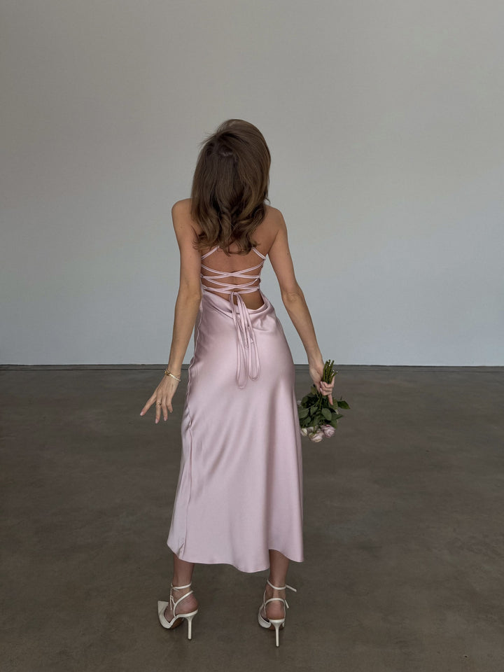 Dusty pink silk satin slip dress, full-length back view: open lace-up back with long tie ends, fluid bias-cut midi skirt and ivory strappy heels.