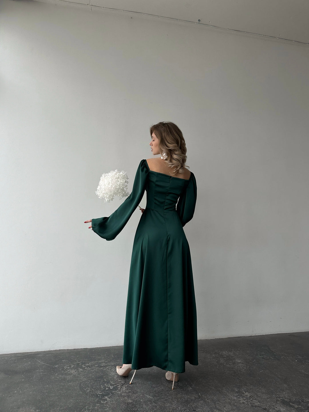 Woman wearing an elegant emerald green long-sleeve maxi dress with a sweeping skirt and thigh slit. A luxurious jewel-toned choice for an upscale holiday cocktail party.