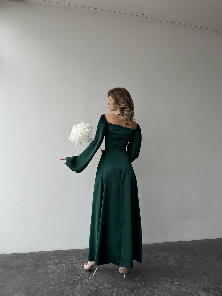 Woman wearing an elegant emerald green long-sleeve maxi dress with a sweeping skirt and thigh slit. A luxurious jewel-toned choice for an upscale holiday cocktail party.