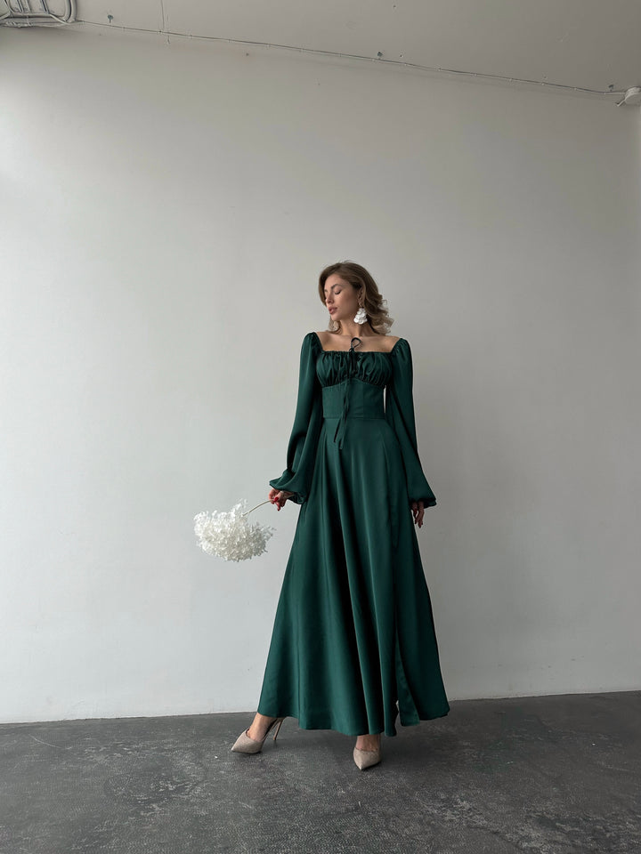 Premium emerald green satin dress offering a flattering fitted waist, long cuffed sleeves, and a maxi-length slit skirt. A modern aspirational look for a luxury gala.