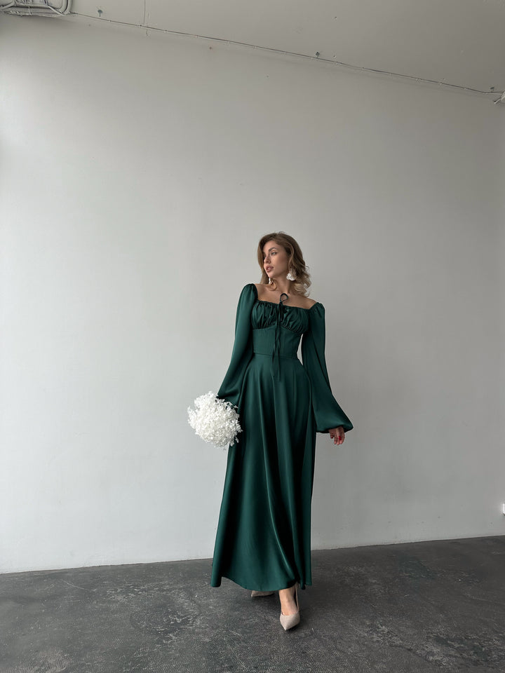 Classic emerald green long-sleeve formal maxi dress made from silky satin. Features an elegant leg slit, perfect for a chic cocktail reception.