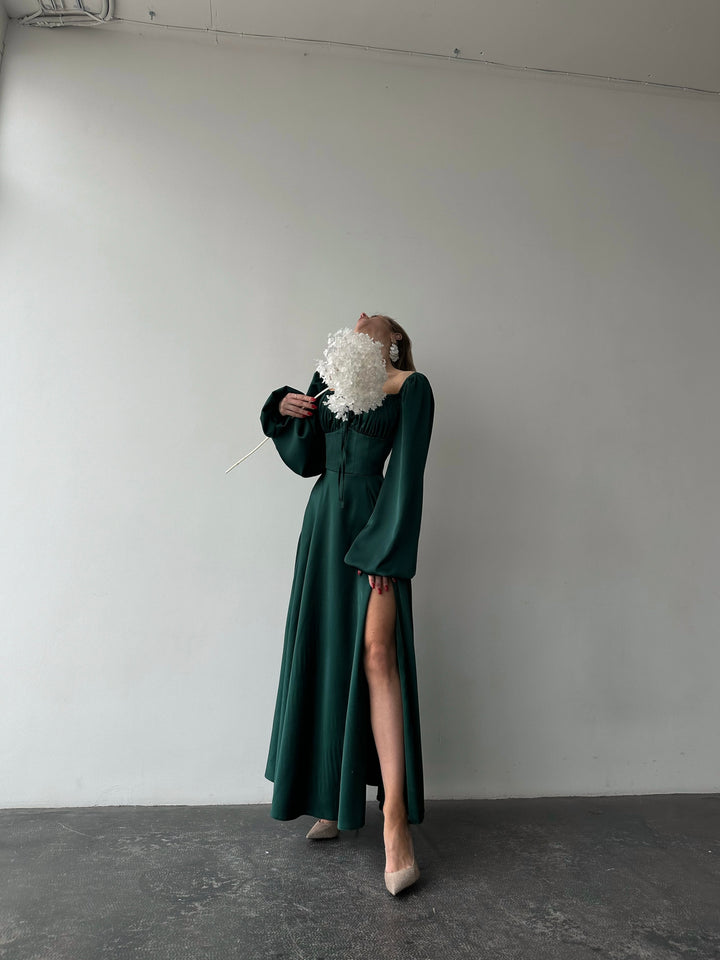 Stunning emerald green silk maxi dress featuring long bishop sleeves and a side slit. A sophisticated choice for a fall wedding guest outfit.