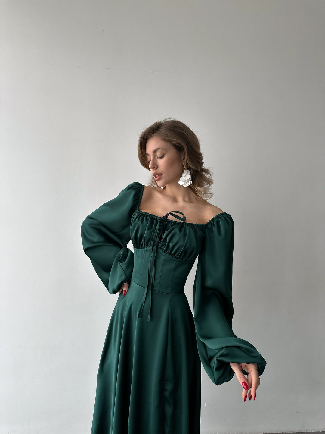 Woman modeling a bold emerald green silk maxi gown with voluminous sleeves and a thigh-high slit. A luxurious look for an evening reception.