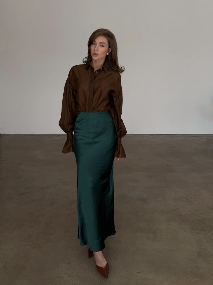 Front profile of a dark emerald bias-cut slip skirt showing the straight column silhouette falling to the ankle.