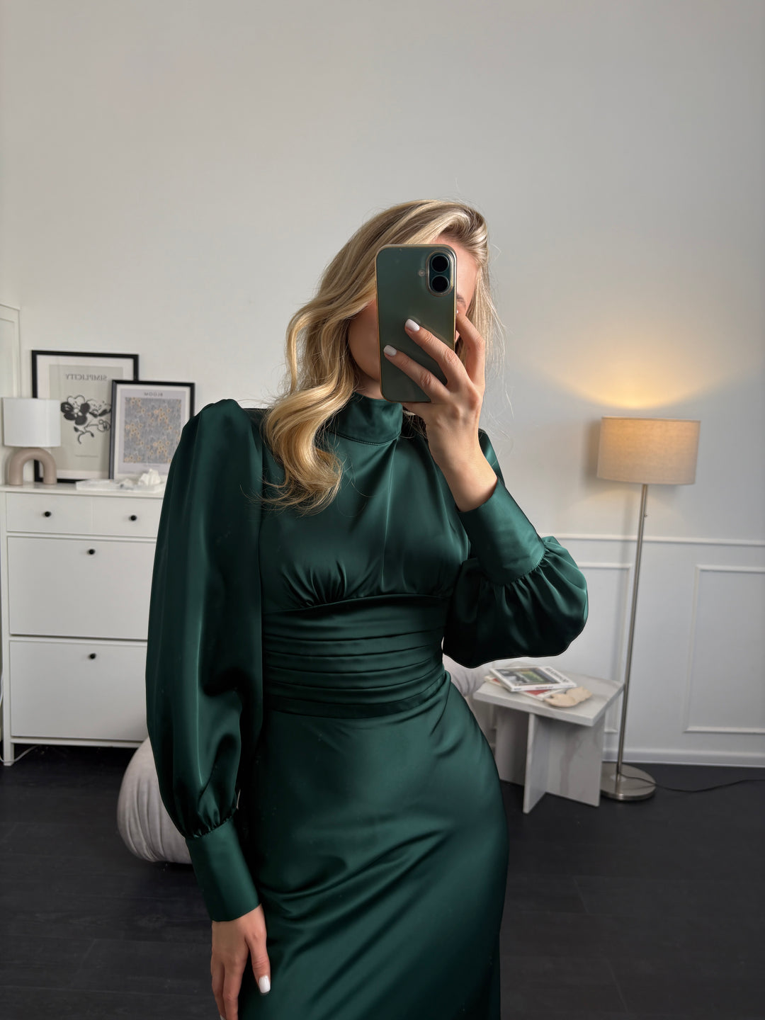 Person wearing an emerald green dress taking a mirror selfie in a room.