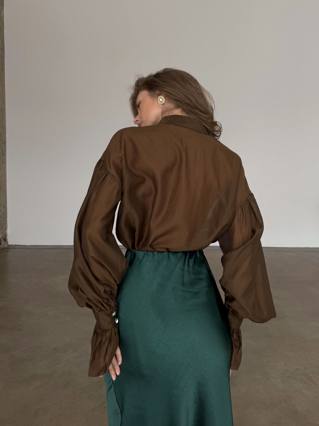 Back view of the model in the studio, showing the fluid movement of the dark emerald skirt and the tucked-in brown blouse.