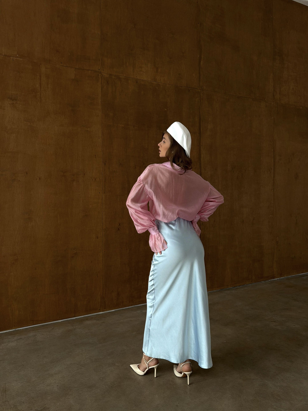 Back view of ice blue satin midi skirt on model showing the clean fall of the satin fabric from the elastic waistband through the hips to the ankle-length hem