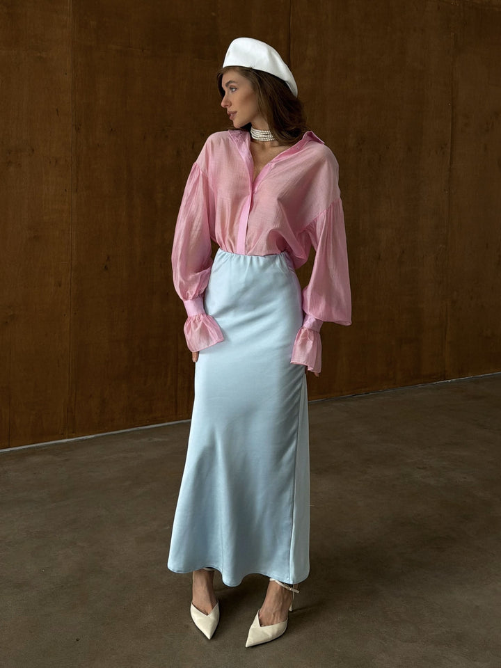 Ice blue satin midi skirt styled with a tucked-in blouse in a studio setting, showing a complete outfit look with heels and minimal accessories