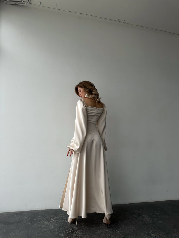 Ivory silk satin maxi dress back view, model looking over shoulder — bishop sleeves, fitted back, floor-length skirt. Perfect for brides, elopements, bridesmaid looks, and formal black-tie events.