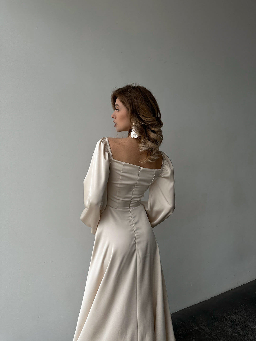 Ivory silk satin maxi dress three-quarter back view — bishop sleeves off the shoulder, high leg slit, romantic silhouette. Perfect for elopements, bridal shoots, wedding receptions, and black-tie evenings.