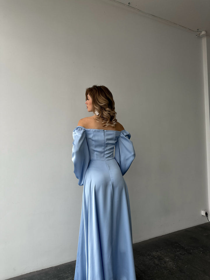 Woman modeling a trendy ice blue silk maxi gown with voluminous sleeves and a thigh-high slit. A luxurious look for a sophisticated evening reception.