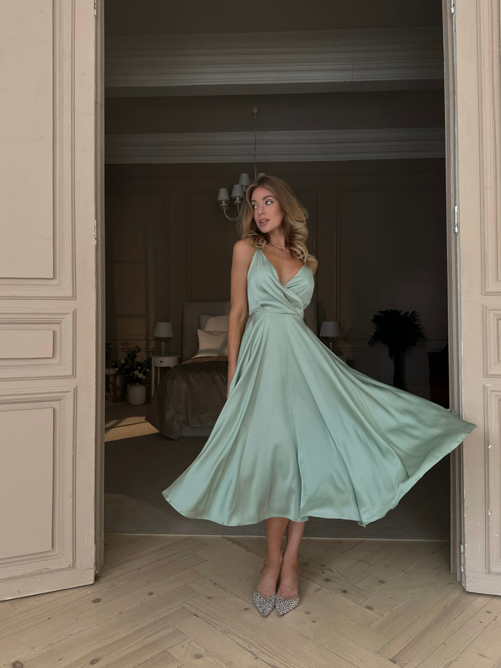 Pistachio green silk satin midi dress with open bow back — movement shot