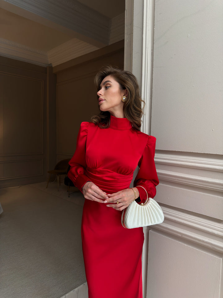 Red satin dress front close-up: mock neck, gathered bodice above a horizontal pleated waistband, puff shoulders and long sleeves with buttoned cuffs.