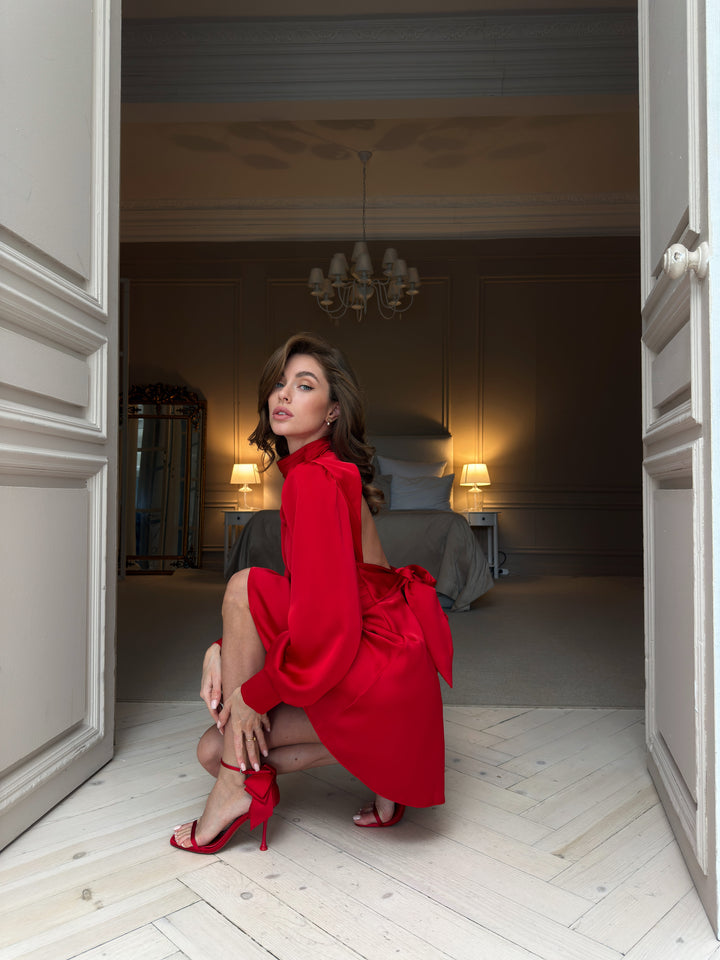 Red silk satin mini dress, side-back view showing the open back below the high collar, oversized waist bow with long tails and voluminous long sleeves.