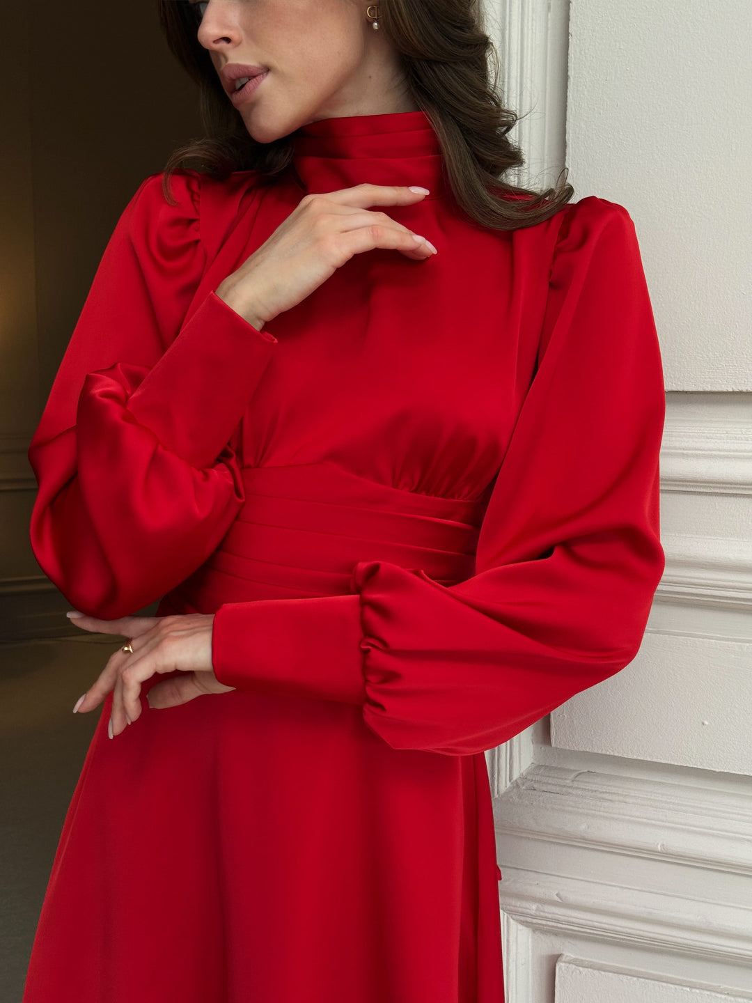 Red silk satin dress close-up: pleated high neckline, long puff sleeves with cuffs, gathered bust and wide pleated waistband above a flared skirt.