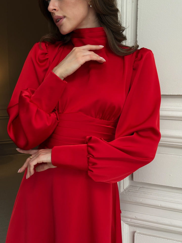 Red silk satin dress close-up: pleated high neckline, long puff sleeves with cuffs, gathered bust and wide pleated waistband above a flared skirt.
