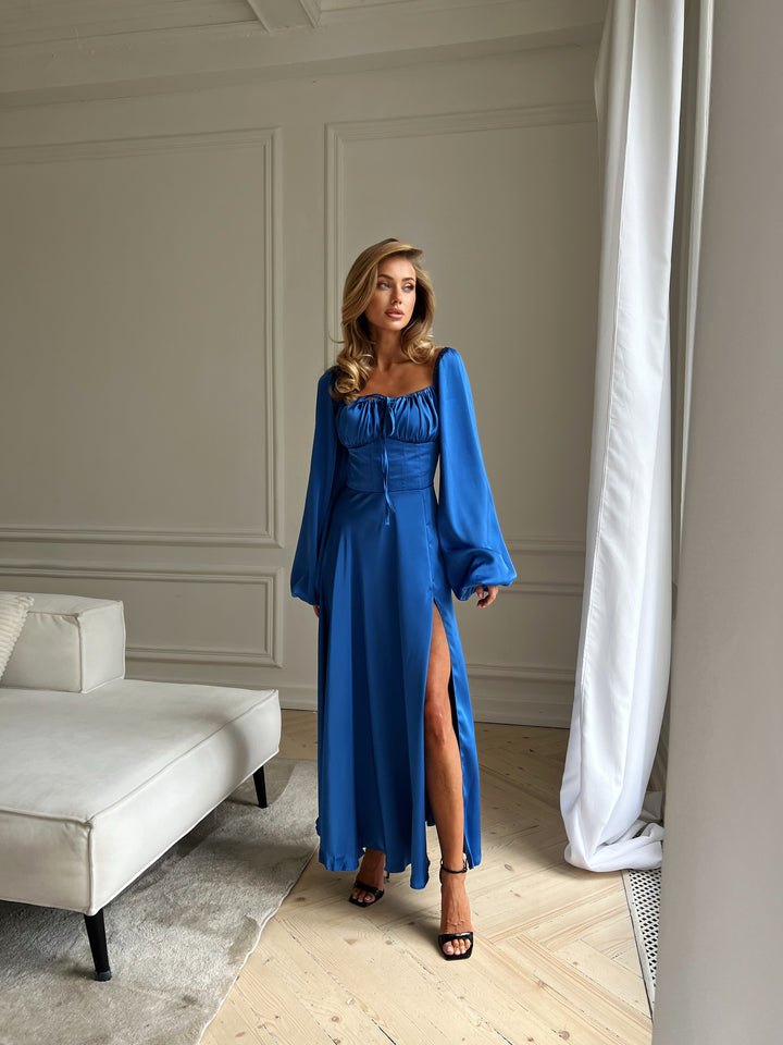 Elegant royal blue silk-like satin dress with a fitted corset waist and flowing maxi skirt with a high slit. Featuring long sleeves and a square neckline. A stunning luxury option for an anniversary dinner or formal holiday party.