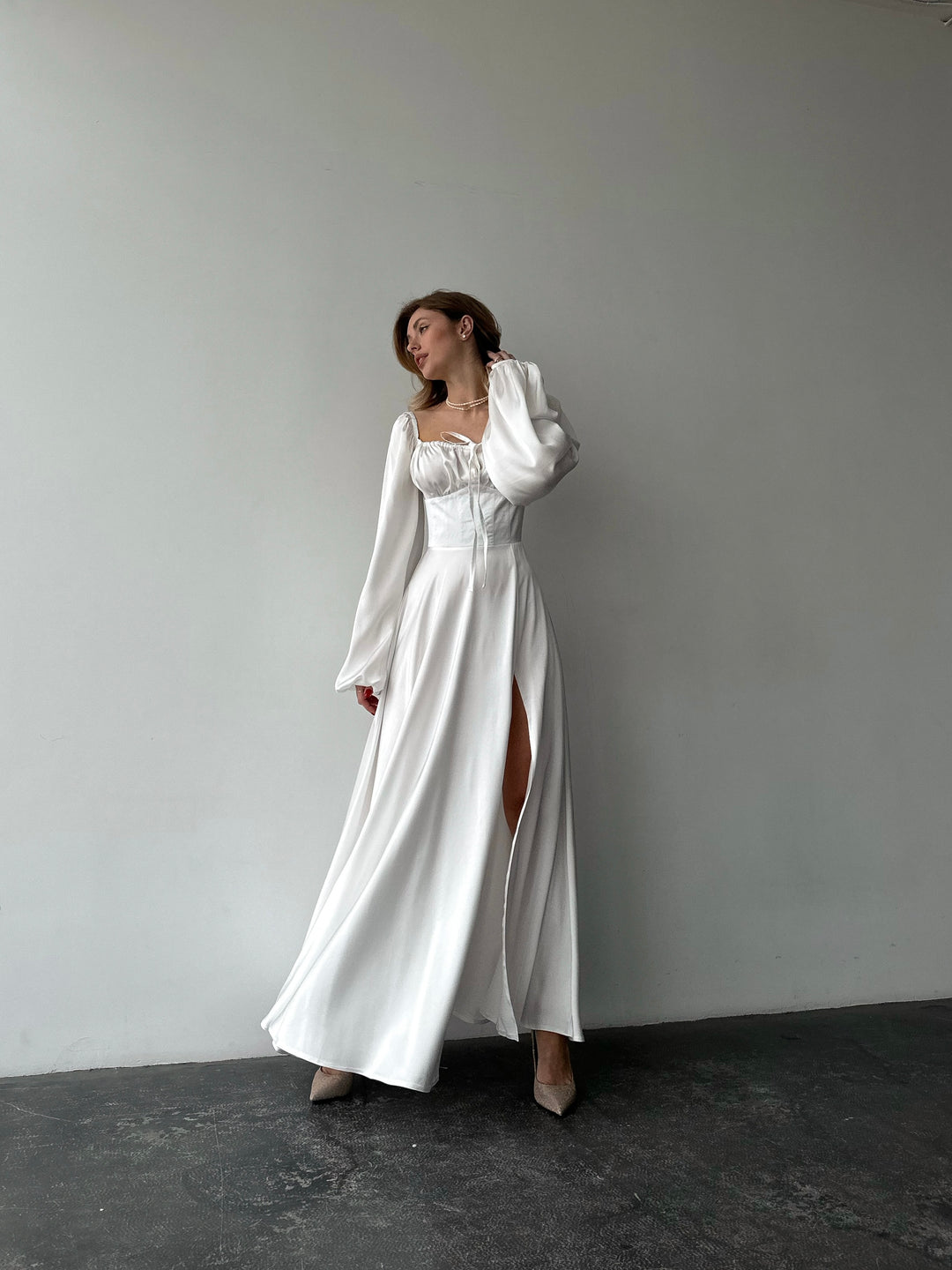 Crisp white long-sleeve evening dress made of smooth satin. Features a structured sweetheart bust and side slit, ideal for a chic NYC style bridal look.