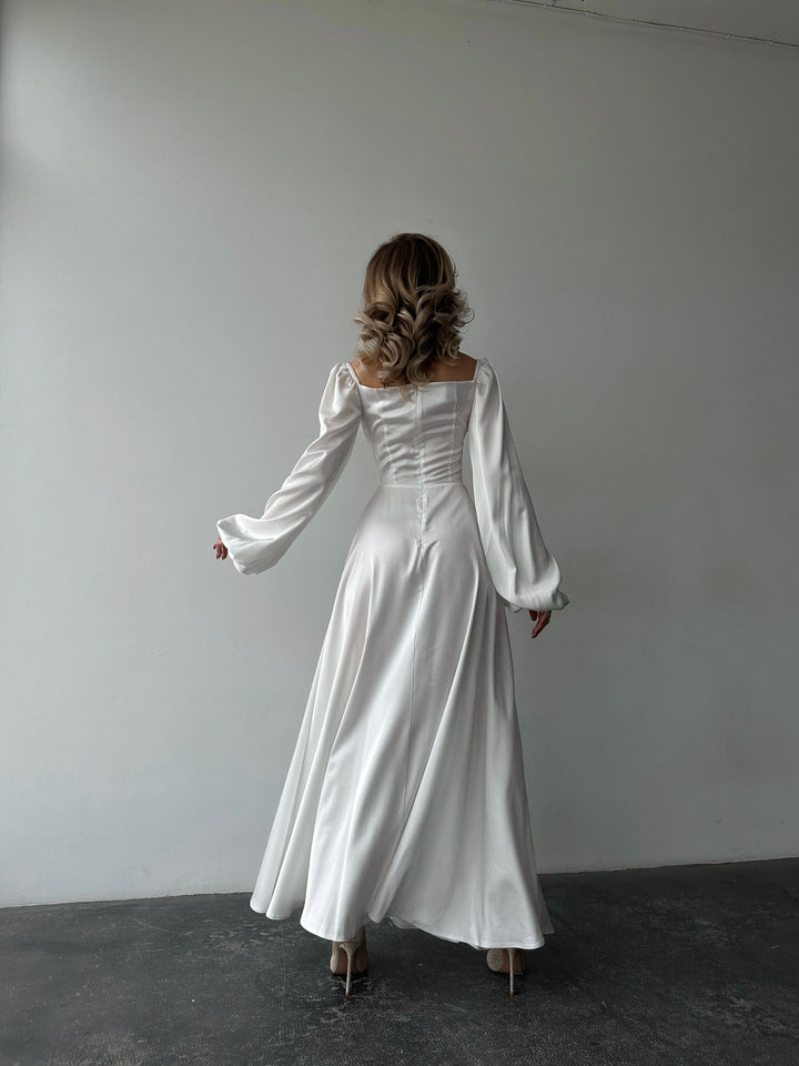 Sophisticated white satin dress offering long cuffed sleeves and a high slit maxi skirt. Perfect for a modern elopement or a formal summer gathering.