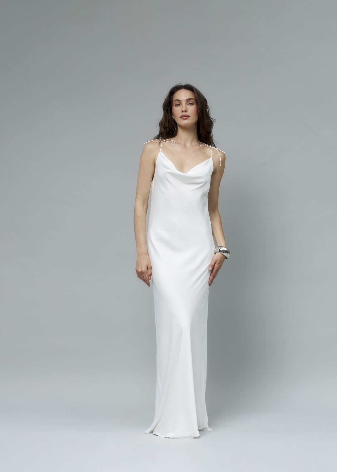 White satin bridal slip dress with bow-tie shoulder straps, model standing arms behind back, full length front view