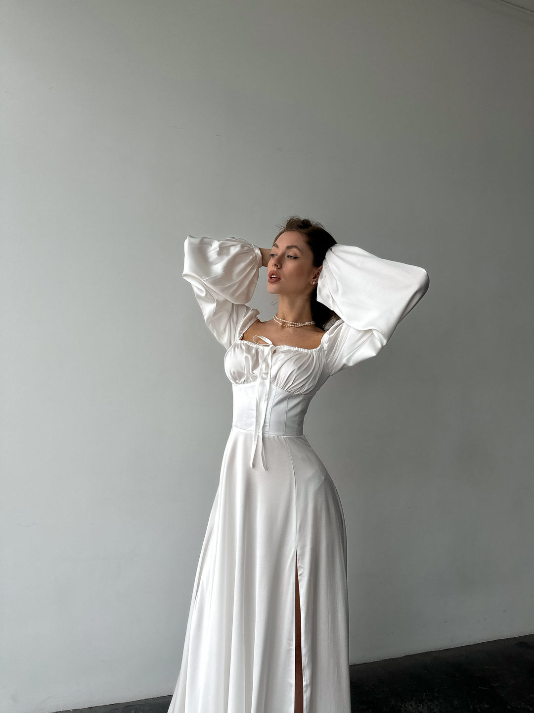 Long-sleeve white silk-blend formal dress highlighting a fitted bodice and sweeping maxi skirt. Ideal for an upscale rehearsal dinner or bridal event.