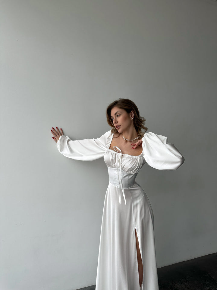 Woman modeling a timeless white silk maxi gown with voluminous sleeves and a thigh-high slit. A luxurious look for a sophisticated Miami vacation outfit.