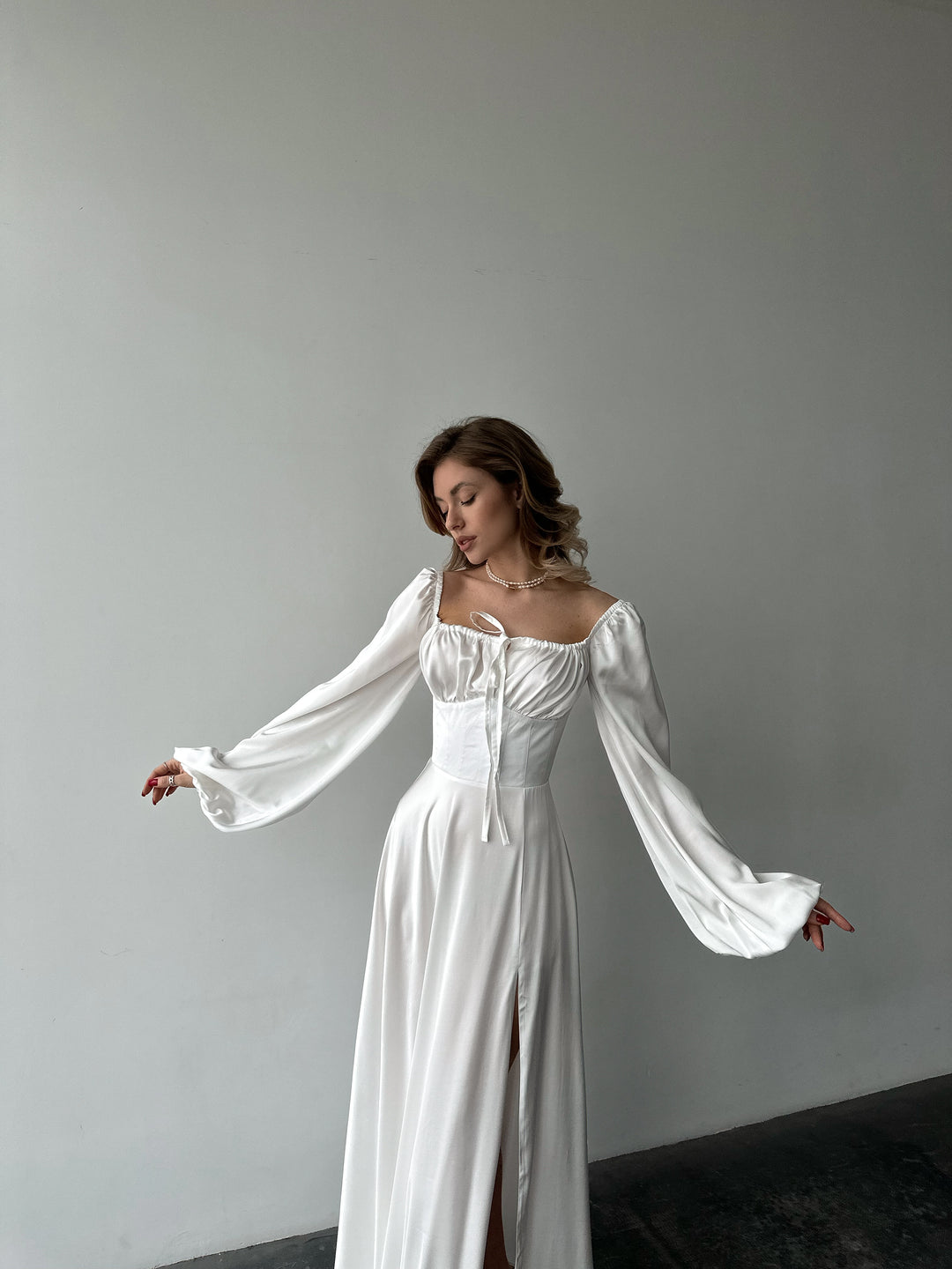 Flowing white satin gown with off-the-shoulder balloon sleeves and a dramatic high slit. A refined and modern option for a destination elopement outfit.